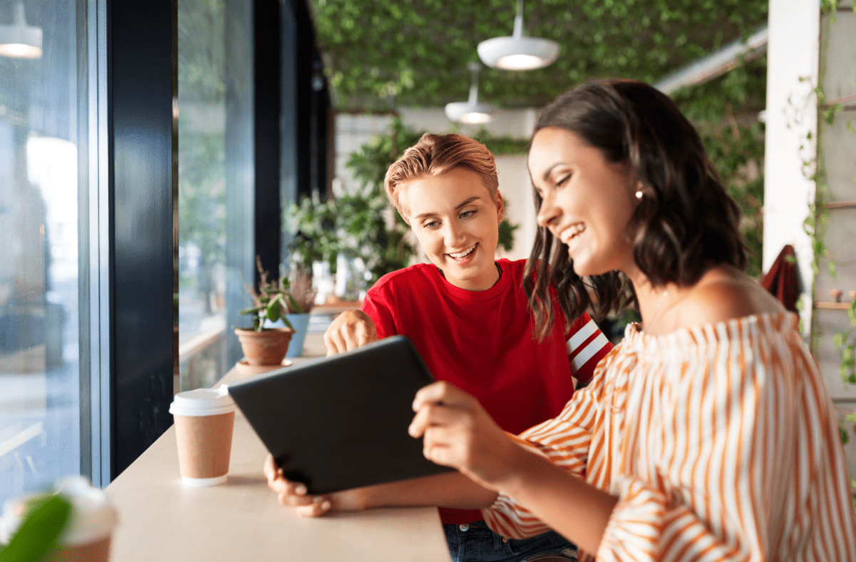 Two women looking at a tablet and discussing insurance at a coffee shop