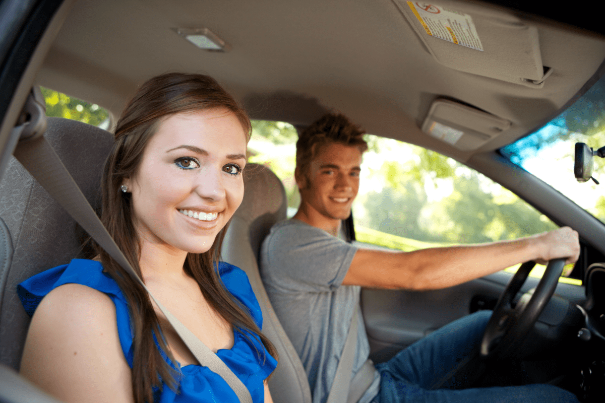 A teenage boy in the driver's seat of a car with a teenage girl in the passenger seat.