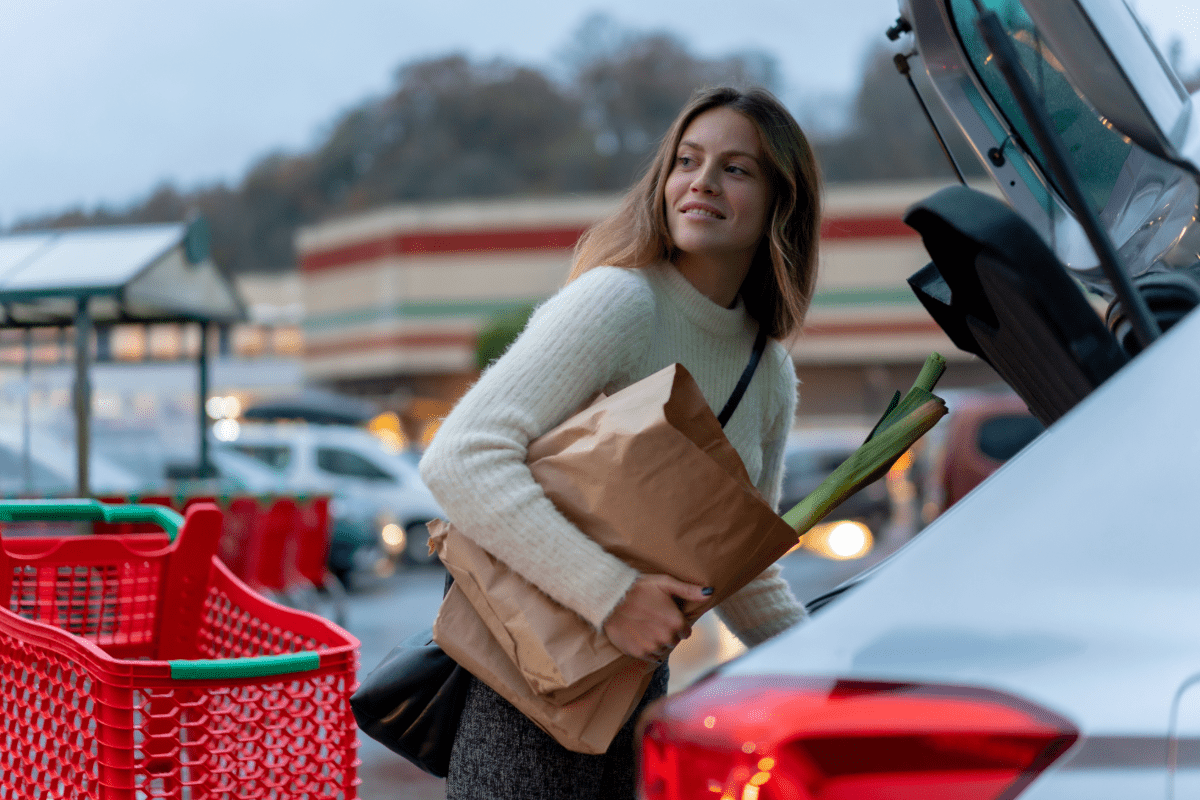 Woman loading groceries into car in business parking lot.