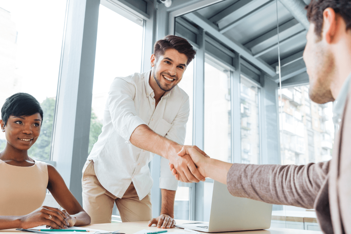 Man shaking another person's hand from across the table after a business meeting.