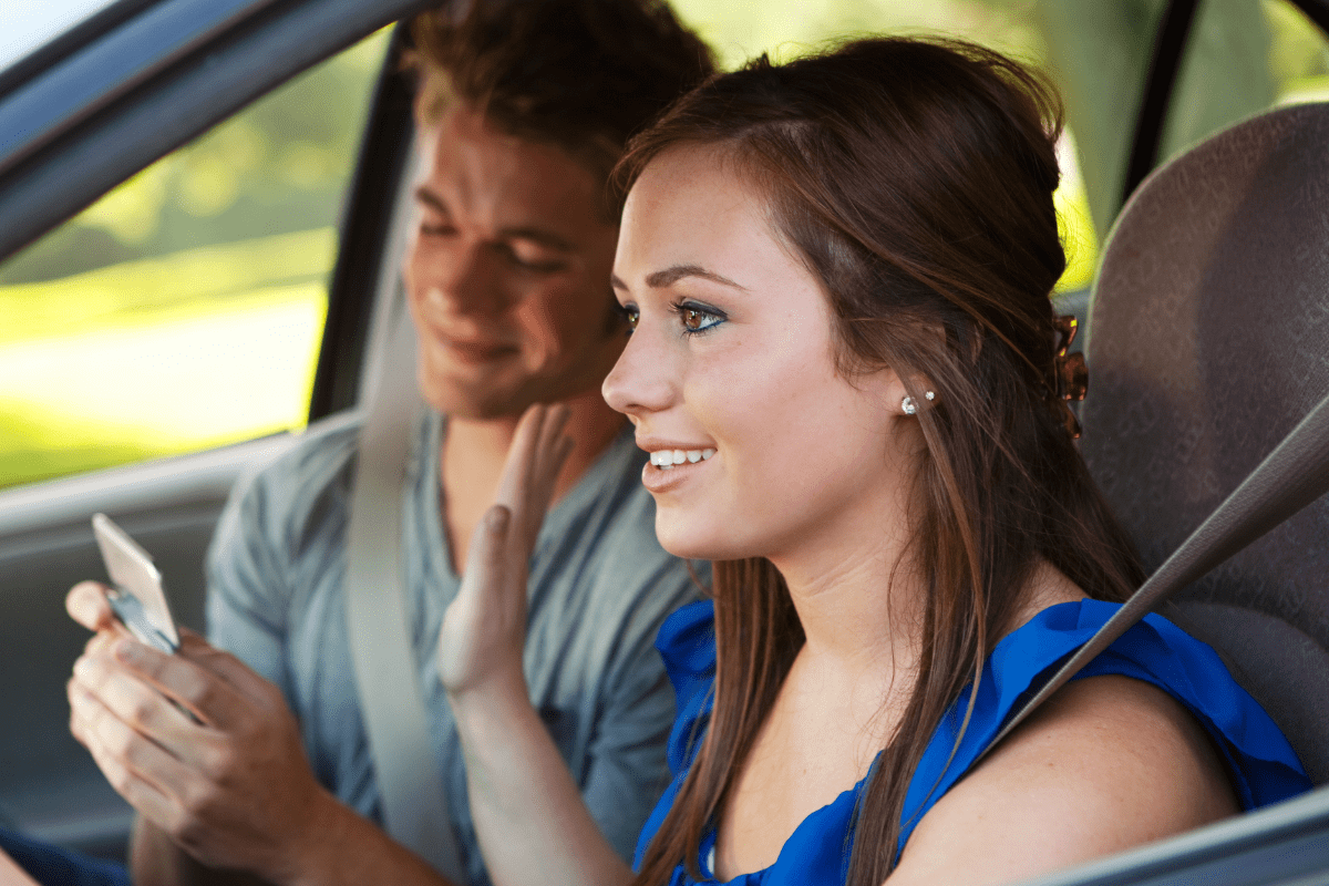 Female teen driver ignoring teenage boy on phone in passenger seat.