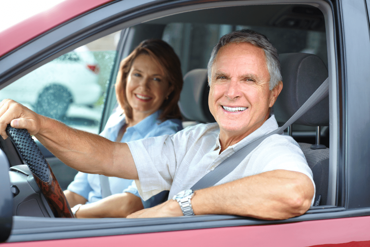 Retired couple smiling in the front of a car.