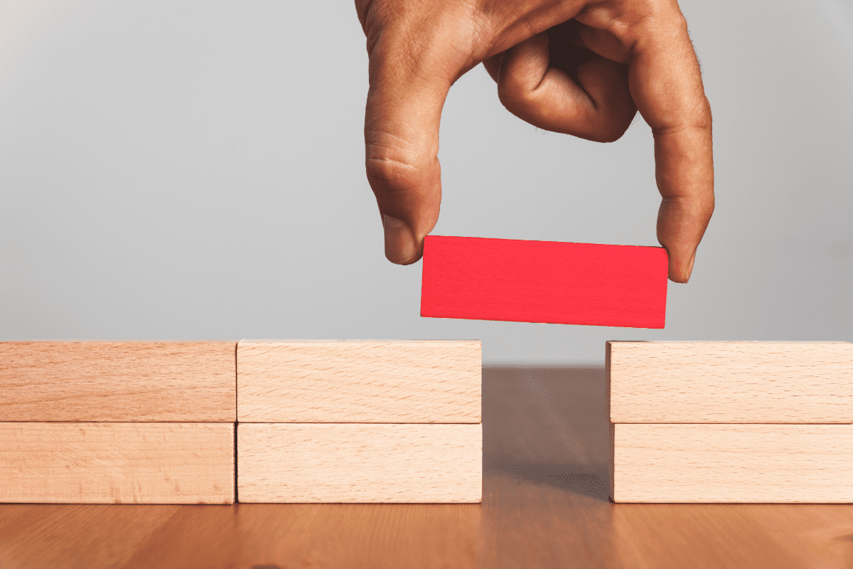 Pile of blocks with gap with hand placing red block to mind the gap.