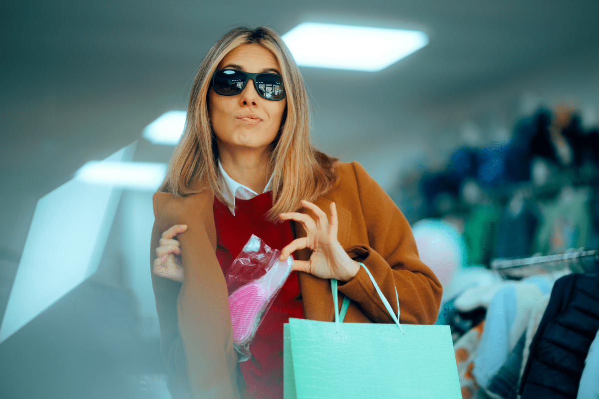 Woman in sunglasses hiding a product in her jacket in an attempt to steal from business.