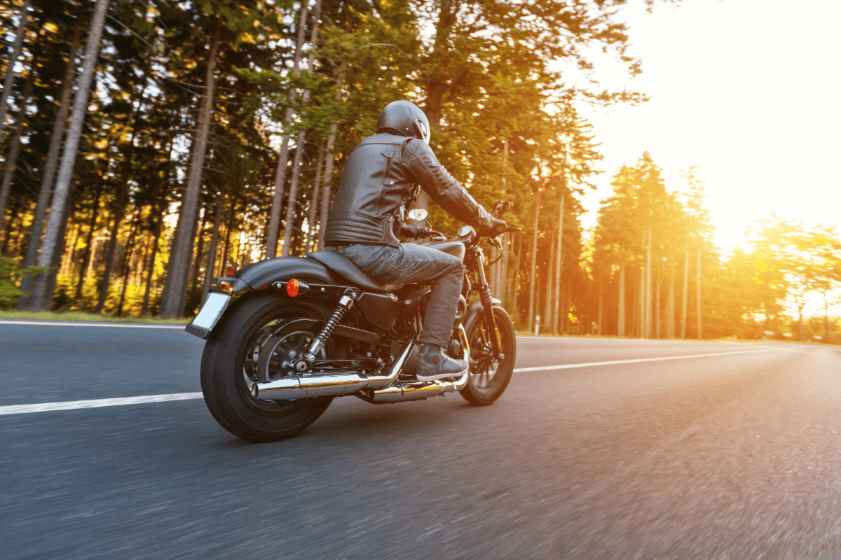 Man riding motorcycle down a wooded road.